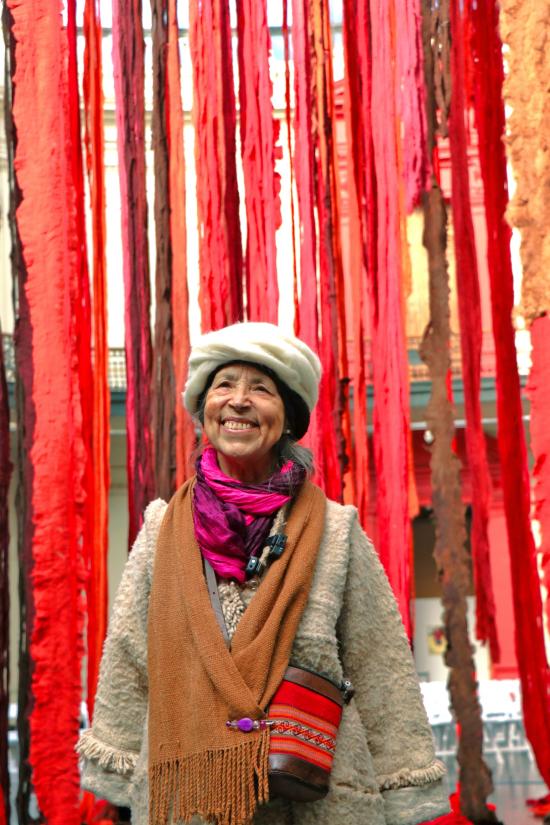 Fotografía de la artista Cecilia Vicuña junto a su instalación Quipu menstrual